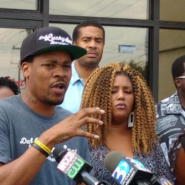 Shaun Corbett and fellow business owners and nonprofit leaders talked to reporters Friday afternoon outside his barber shop, Da Lucky Spot, on North Tryon St. (David Boraks/WFAE)